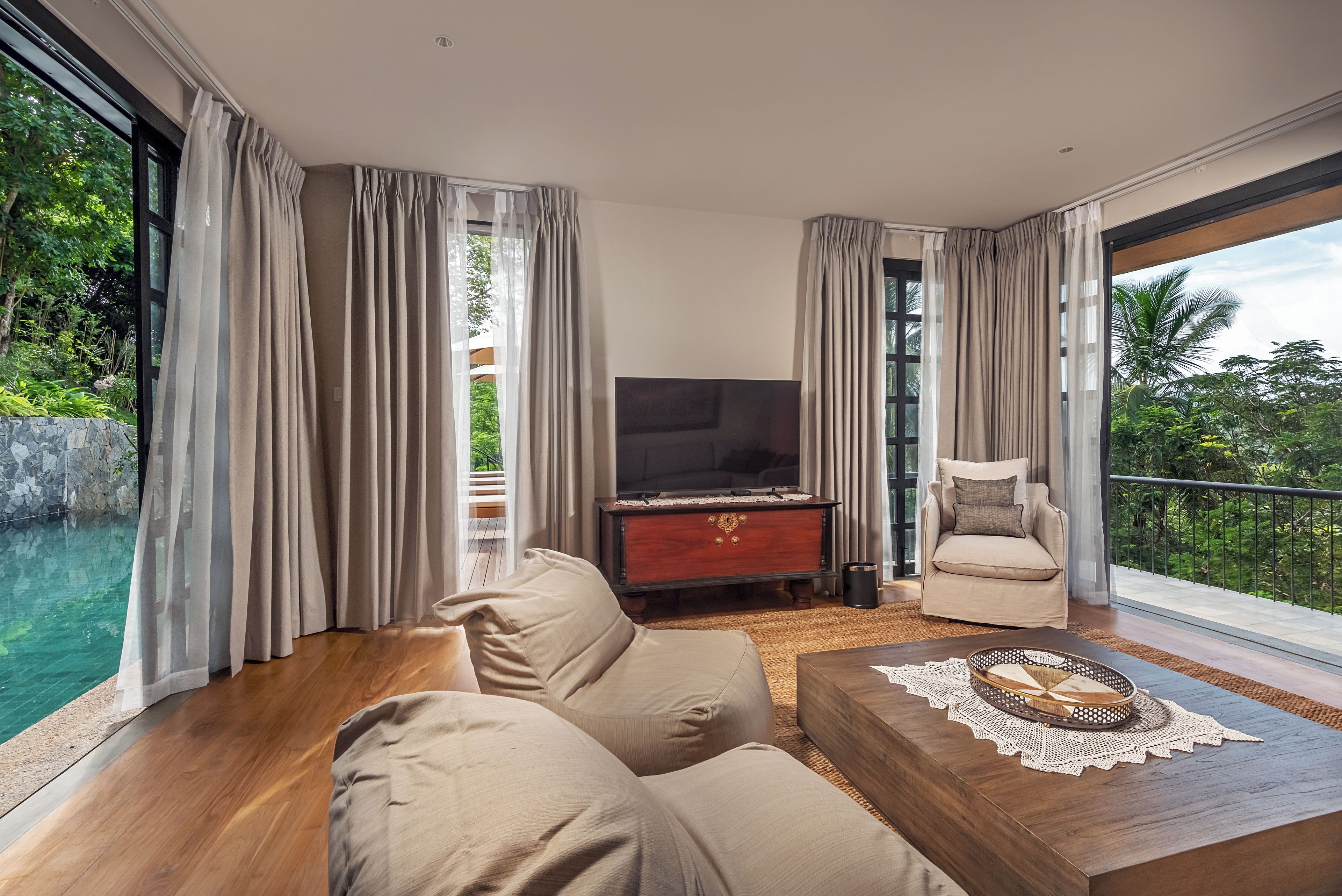 Ein modernes Wohnzimmer mit einer Couch, einem Fernseher und Blick auf einen Pool und Grünflächen.