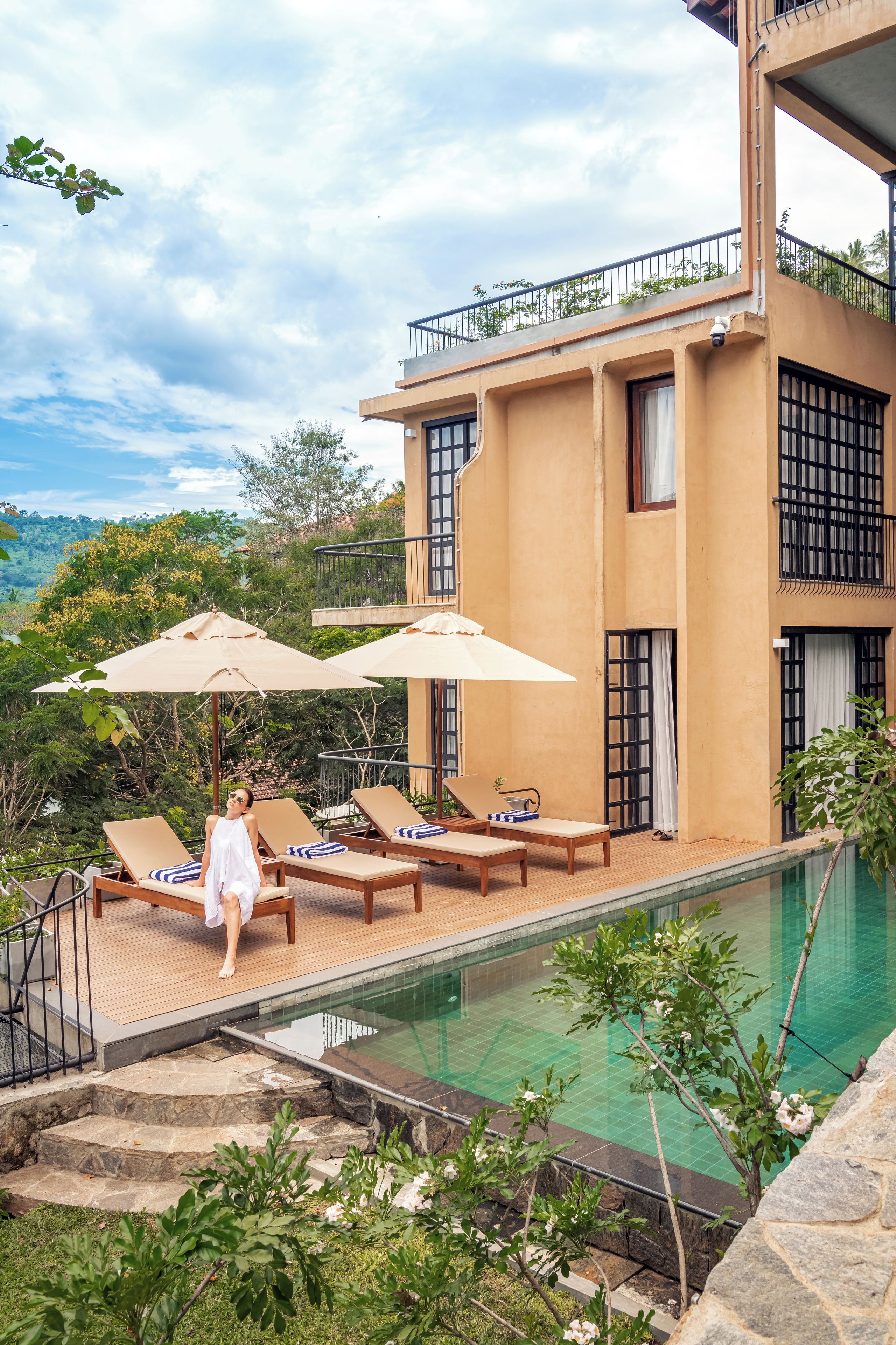 A modern building with a pool, lounge chairs, and umbrellas.