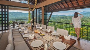 Un comedor con una mesa preparada para cuatro, con vistas a un paisaje exuberante con montañas y vegetación.