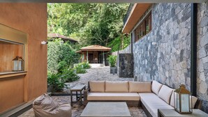 A cozy outdoor seating area with a sofa, coffee table, and bean bag, surrounded by stone walls and greenery.
