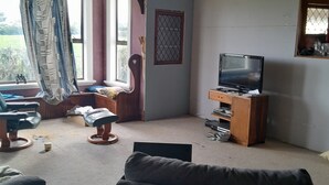 Un soggiorno con un divano, una televisione su un mobile in legno, una finestra con tende e un tavolino con una lampada.