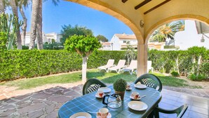 An outdoor patio with a table set for two, surrounded by a garden with a hedge and palm trees. - Bungalow in Denia 3 minutes from the beach with air-conditioning (Denia)