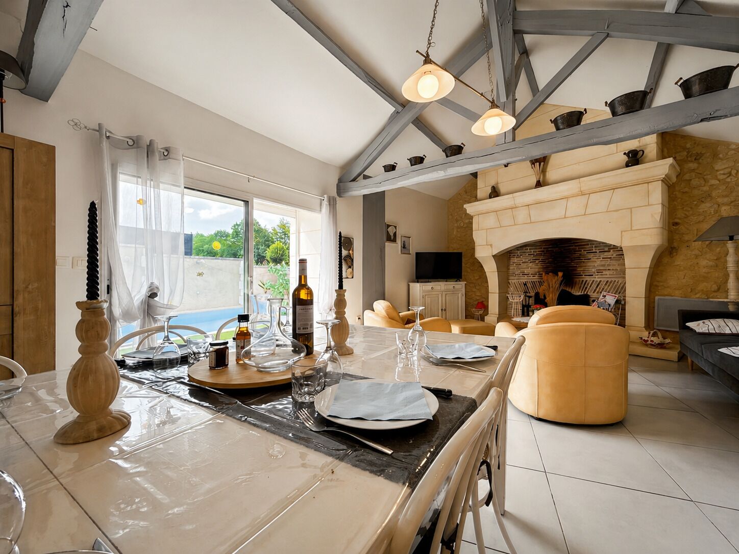 Ein geräumiges Wohnzimmer mit Kamin, eine Essecke mit Tisch für zwei Personen und ein großes Fenster mit Blick ins Freie.