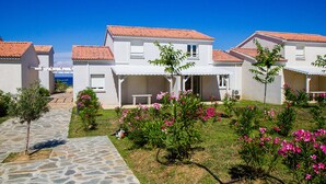 A row of white buildings with red-tiled roofs, a stone pathway, and pink flowering plants. - Villa Climatisée T3 Piscine Chauffée Accès Direct à la Plage de Prunete (Cervione)