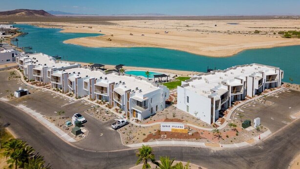 Een modern resort met witte gebouwen, een zwembad en een woestijnlandschap.