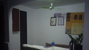A reception area with a counter, a ceiling fan, framed certificates on the wall, and a potted plant. - Max Travellers Inn (Lapu-Lapu)