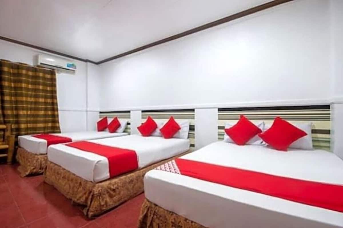 A hotel room with three beds, each with red and white bedding, and a headboard with a striped pattern.