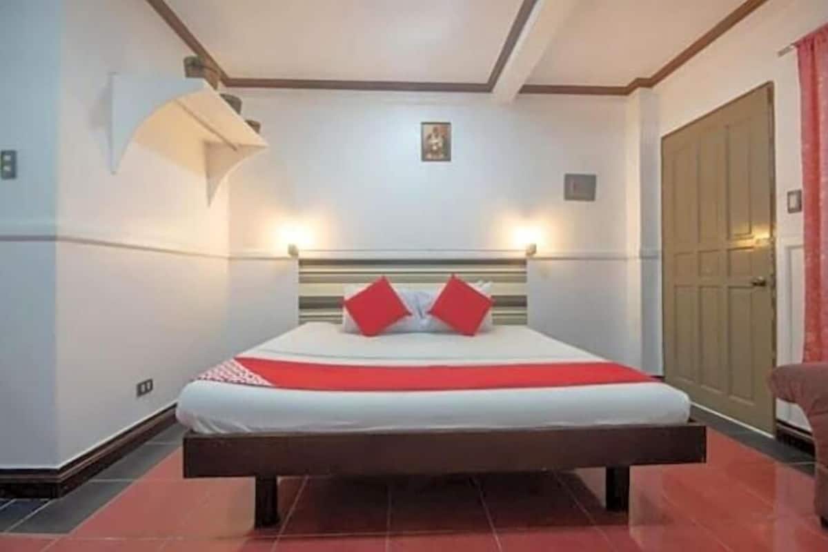 A neatly made bed with a red and white bedspread, a wooden headboard, and two red pillows.