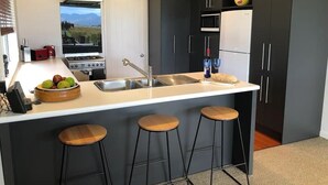 A modern kitchen with a central island, bar stools, a stove, and a microwave. - Ben Morven Vineyard Cottage (Fairhall)