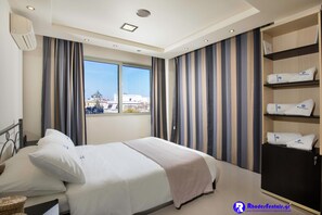 A hotel room with a bed, a wardrobe, a window, and a view of buildings outside. - Rhodes Central Suite (Rhodes)