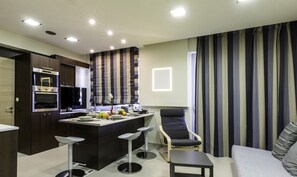 A modern kitchen with built-in appliances, a dining area with bar stools, and a living space with a sofa and striped curtains.