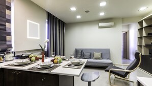 A modern kitchen with a dining area, a grey sofa, and a small table with a chair. - Rhodes Central Suite (Rhodes)