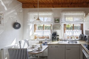 Uma cozinha com área de refeições, teto de madeira, paredes brancas e janela com cortinas.