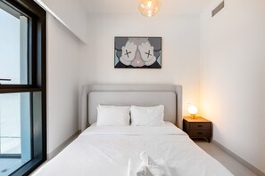 A modern bedroom with a large bed, a bedside table with a lamp, and a framed artwork on the wall.