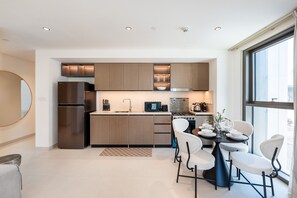 Een moderne keuken met inbouwapparatuur, een eethoek met een ronde tafel en stoelen, en een groot raam dat voor natuurlijk licht zorgt.
