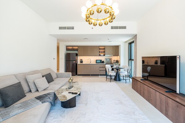 A modern living room with a sofa, coffee table, and a dining area with chairs and a kitchen in the background.