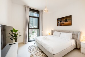 A modern bedroom with a large bed, a TV, a plant, and a window with curtains.