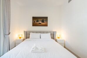 A hotel room with a bed, two bedside tables with lamps, a painting on the wall, and a window with curtains.