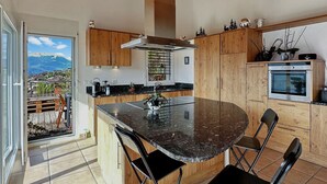 A modern kitchen with a central island, wooden cabinets, and a view of a mountain landscape.