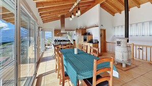 A spacious dining area with a wooden table and chairs, a kitchen in the background, and a balcony with a view.