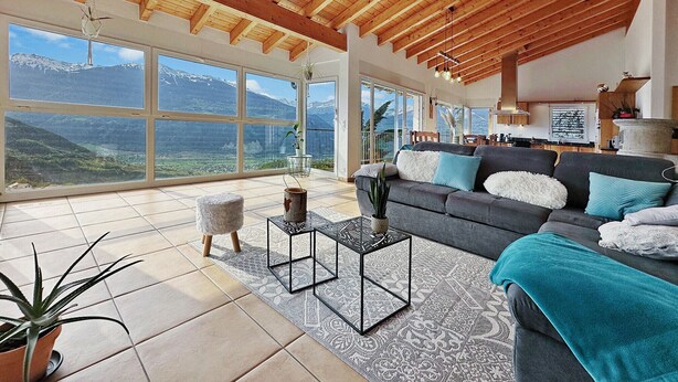 A spacious living room with a large window overlooking a mountainous landscape, a cozy sofa with decorative pillows, and a small side table.