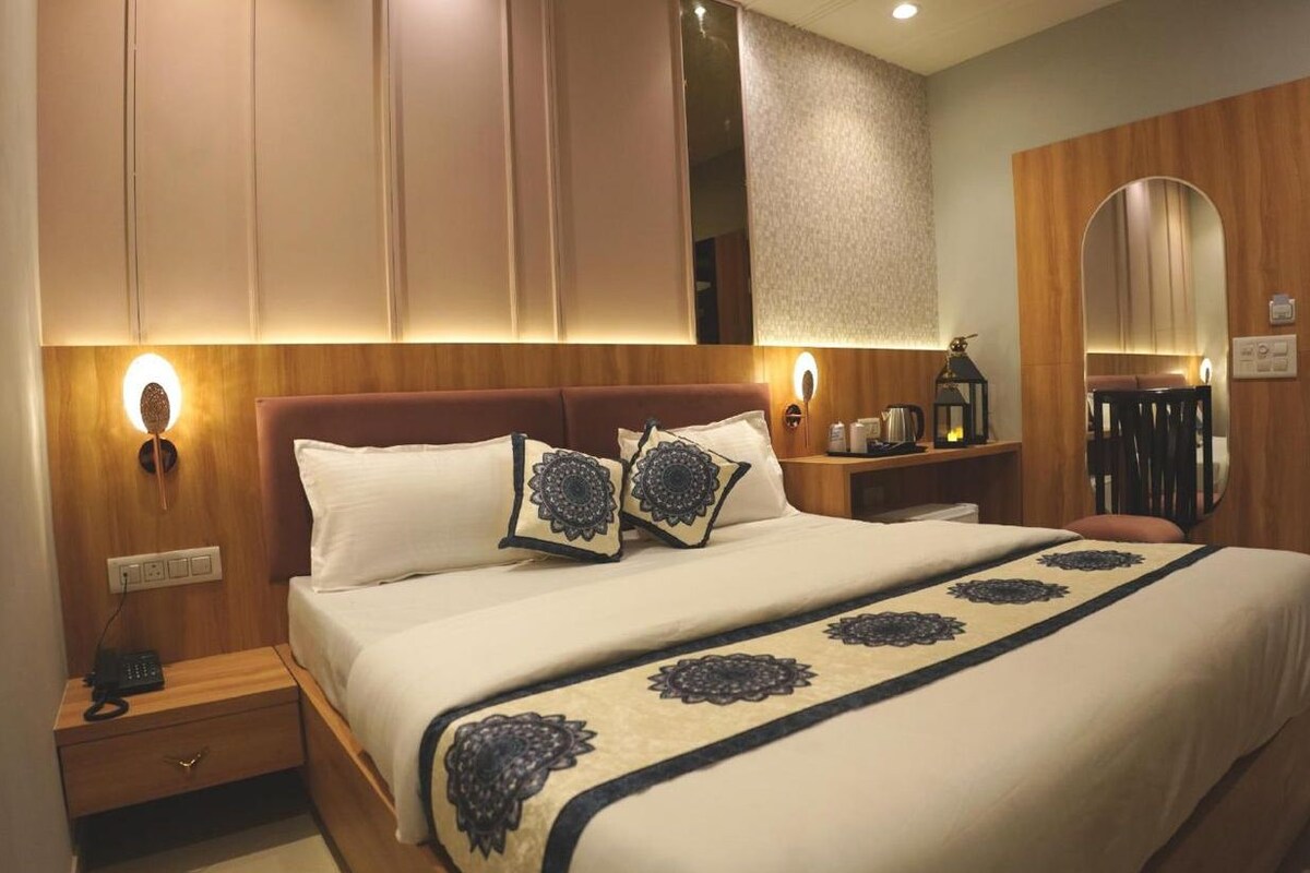 A hotel room with a bed, bedside tables, a nightstand, a mirror, and a wall-mounted light fixture.