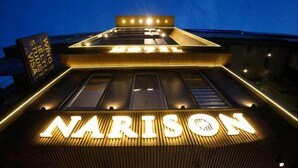 Een gebouw met een opvallend 'NARISON'-bord bij de ingang, verlicht door lampen.