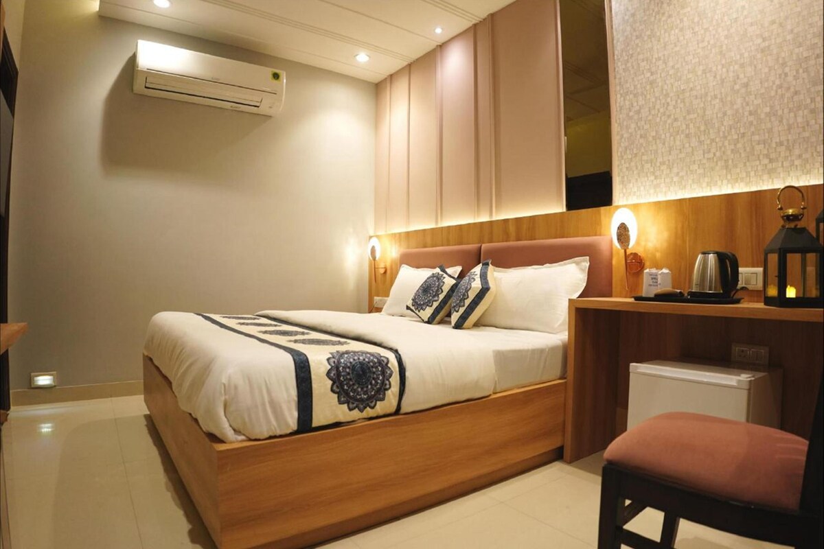 A modern hotel room with a wooden bed, a desk with a lamp, and a small refrigerator.