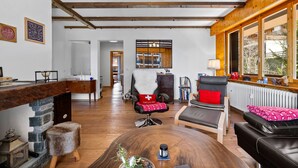 A spacious living area with a stone fireplace, wooden beams, and a large window. - Le Torrent 16 - 6 pers - au calme (Haute-Nendaz)