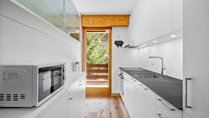 A modern kitchen with white cabinets, a built-in oven, and a large window overlooking a wooden deck. - Le Torrent 16 - 6 pers - au calme (Haute-Nendaz)