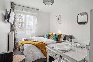Relax in a serene space with a neatly made bed, dining table, and comfortable chair.