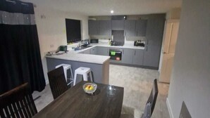 A modern kitchen with grey cabinets, a central island, and a dining area with a wooden table. - Full house- Free Parking, Wifi, and appliances to make your stay comfortable. (Hull)