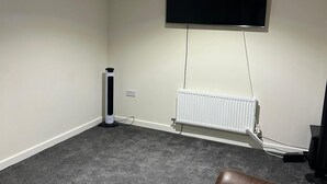 A living room with a brown leather sofa, a flat-screen TV mounted on the wall, a radiator, and a standing heater. - Full house- Free Parking, Wifi, and appliances to make your stay comfortable. (Hull)