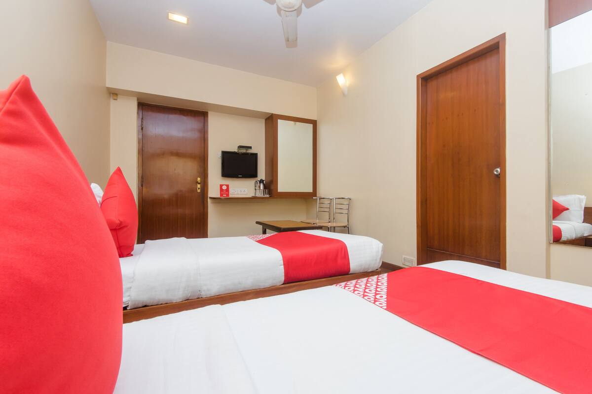 A hotel room with two beds, a TV, a desk, and a mirror.