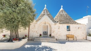 A small stone building with a central door and two conical roofs, surrounded by a gravel area and a tree. - 3856 Trulli Ulivo di Puglia by Barbarhouse (Fasano)