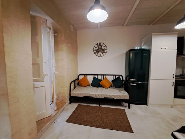 Un espacio habitable pequeño con una cama, un reloj, un refrigerador y una puerta.