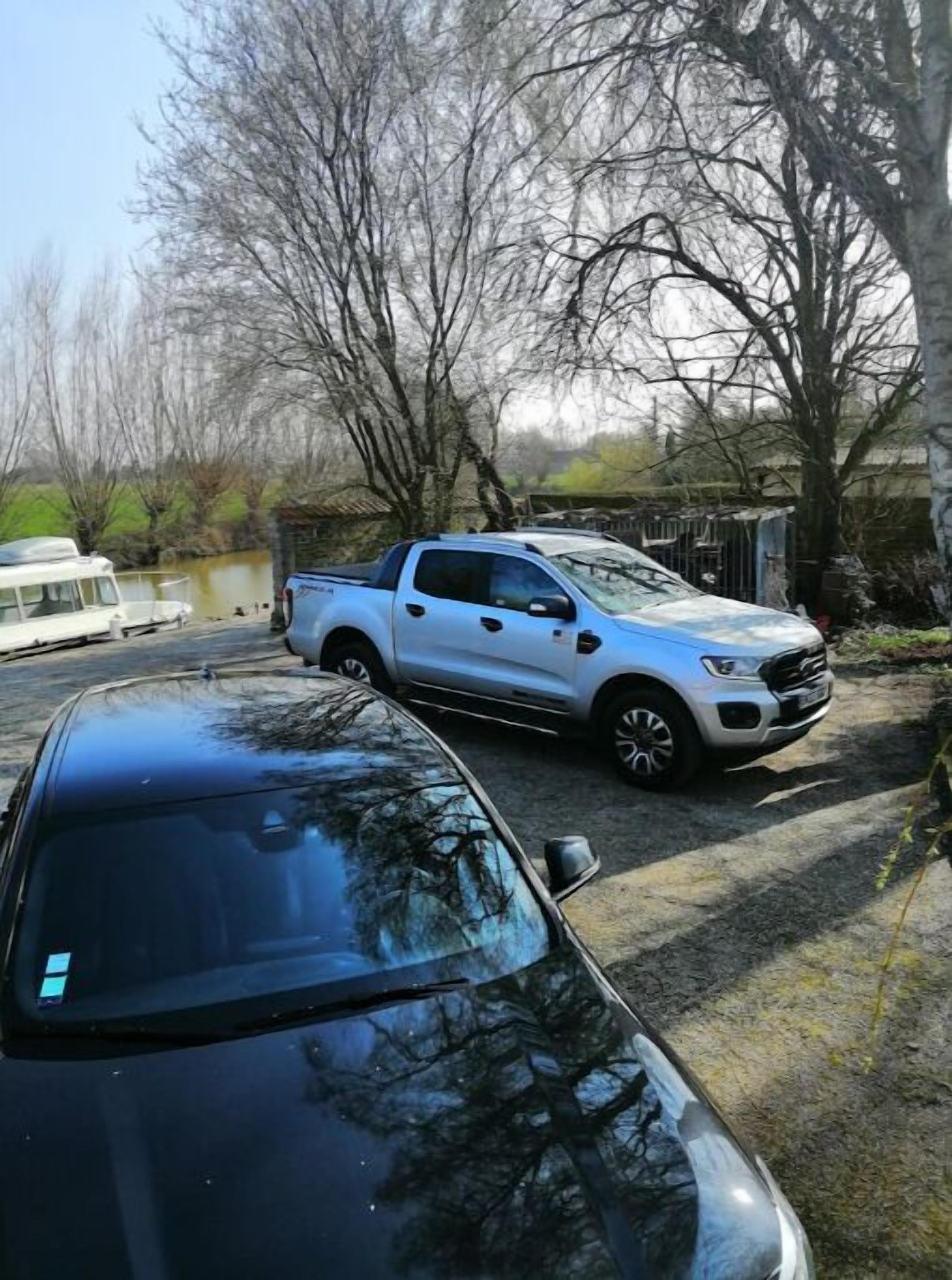 Ein weißer Pick-up auf einem Feldweg, im Vordergrund ein schwarzes Auto.