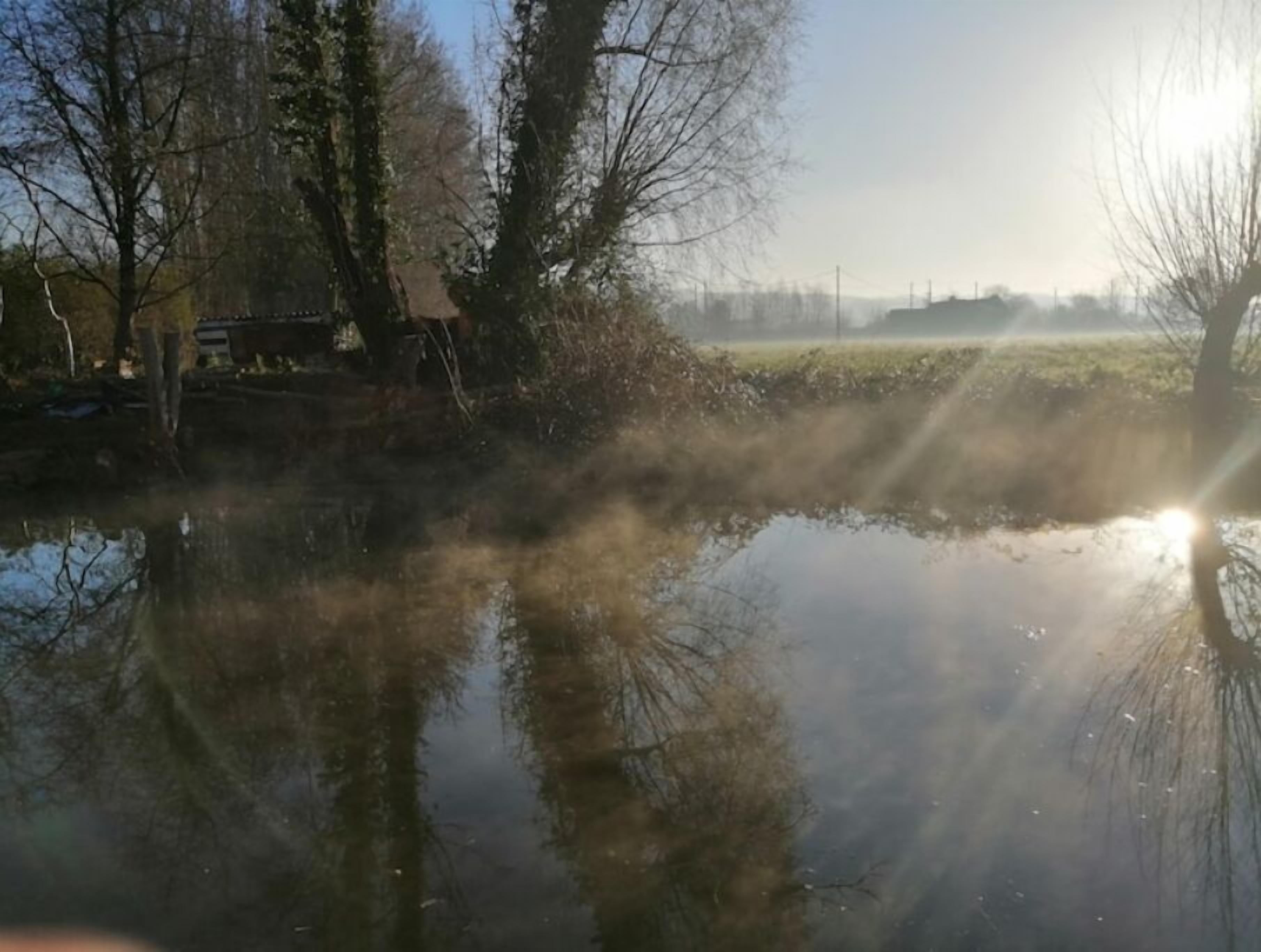 A calm river with trees and a distant building.