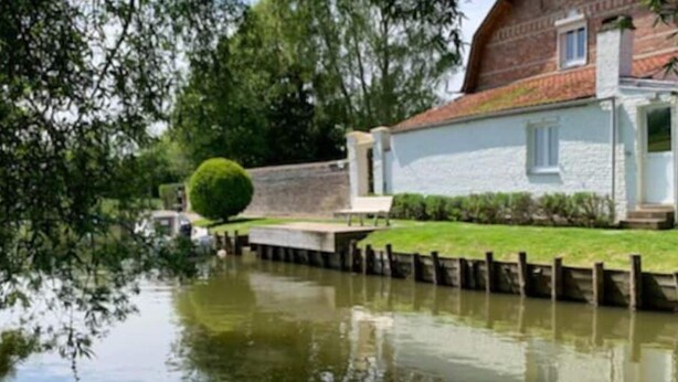 A canal with a stone building on the right, surrounded by greenery.