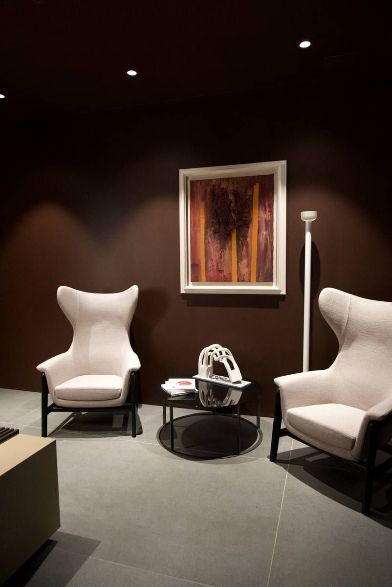 A modern room with two white armchairs, a round table, and a framed abstract painting on the wall.