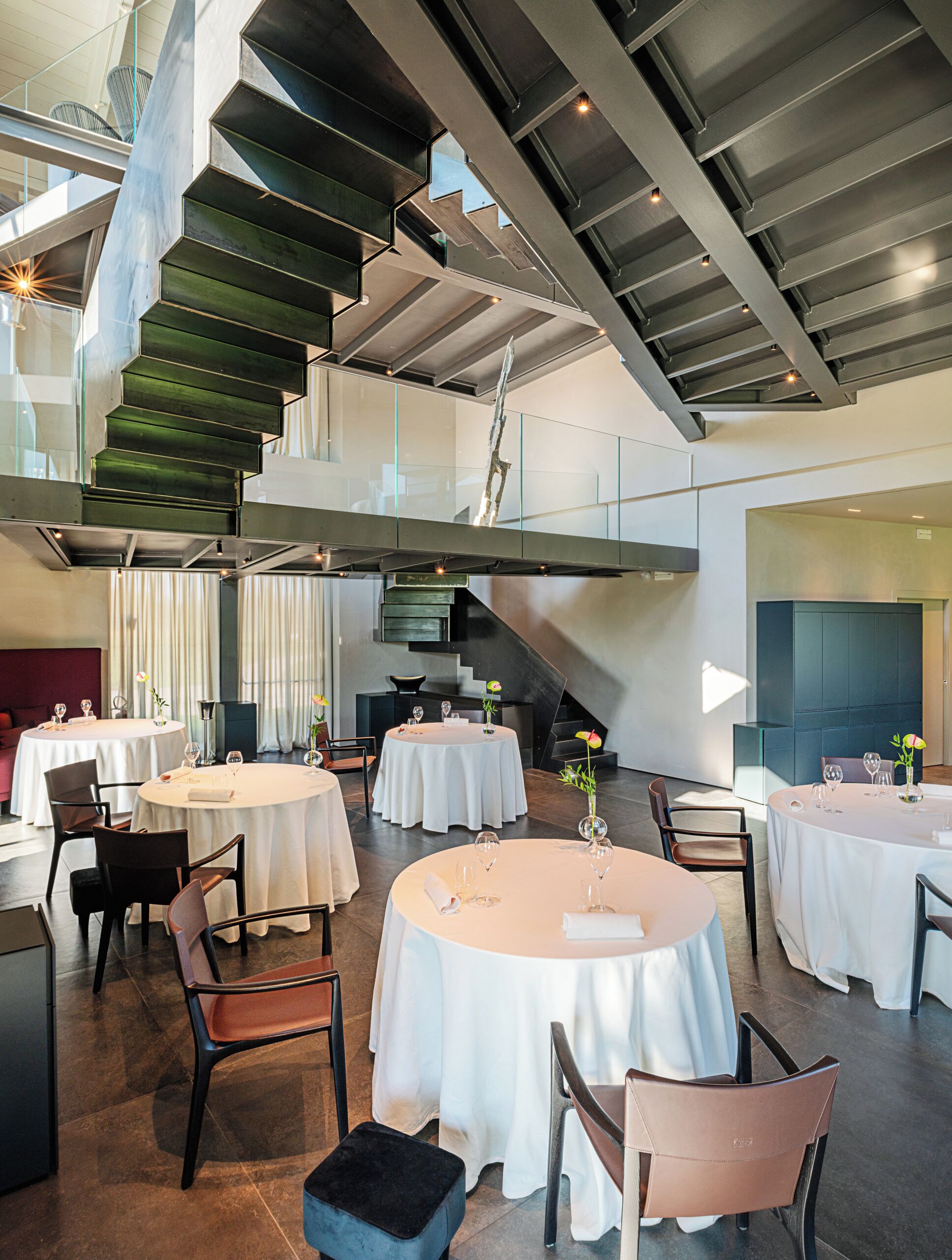 Un espace repas moderne avec des tables rondes, des chaises et un escalier.
