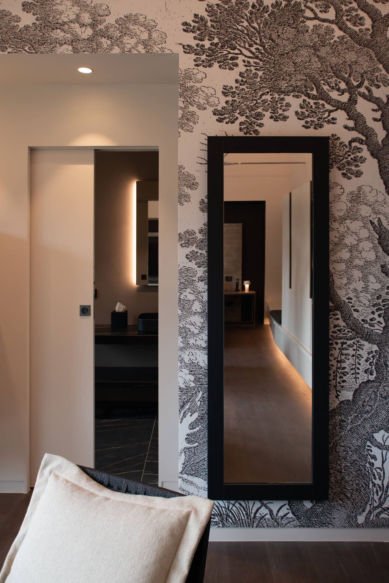 A hallway with a large mirror reflecting a modern interior. A plush white pillow is visible in the foreground.