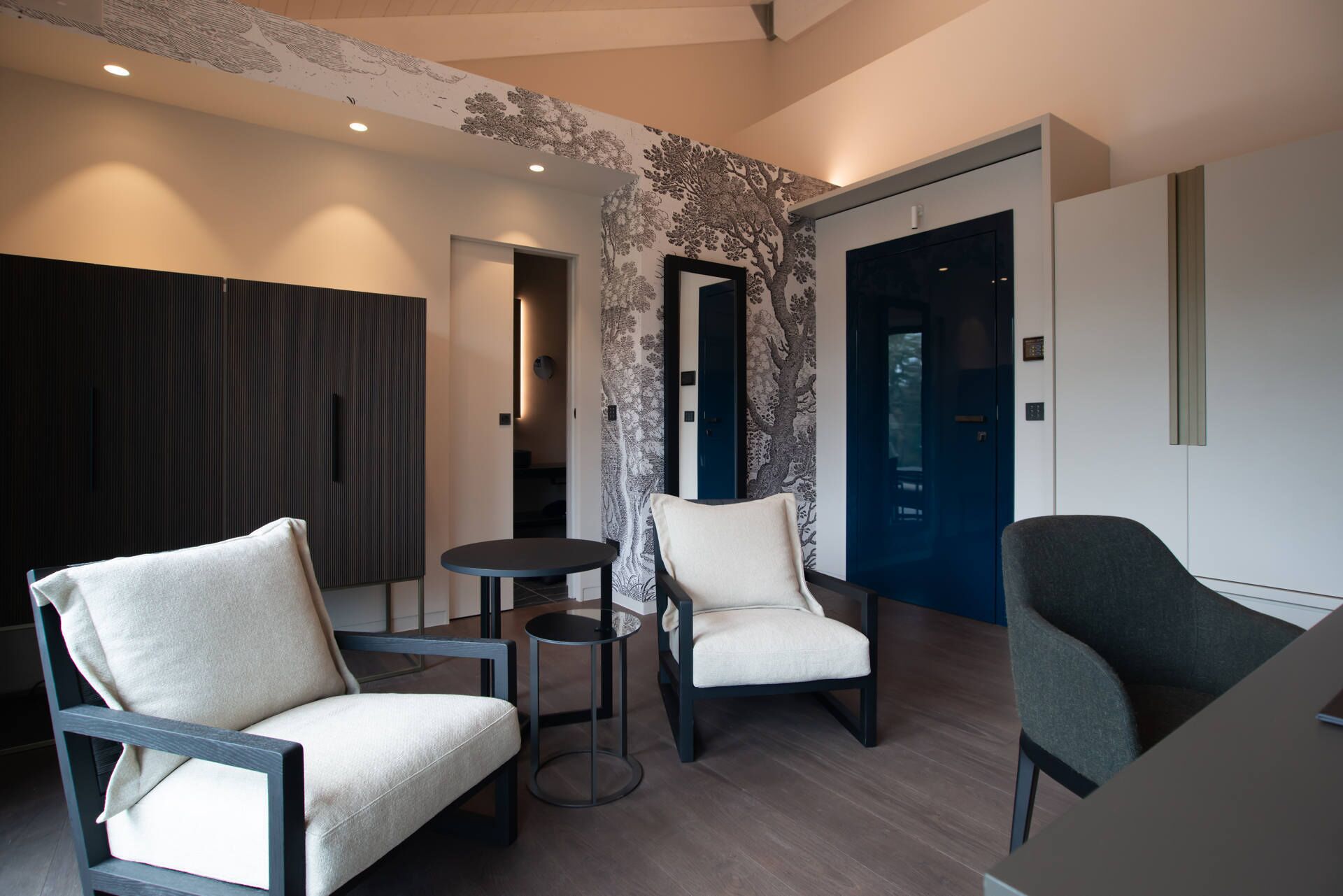 Une chambre d’hôtel moderne avec deux fauteuils, une petite table ronde et une porte bleue.