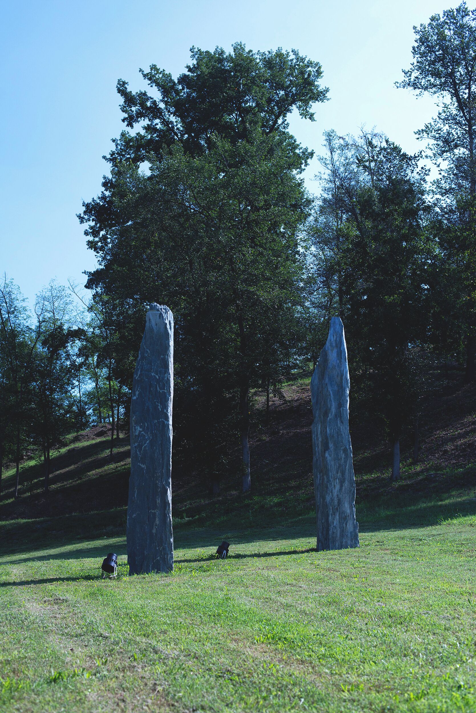 Two tall stone monoliths in a grassy field with trees in the background.