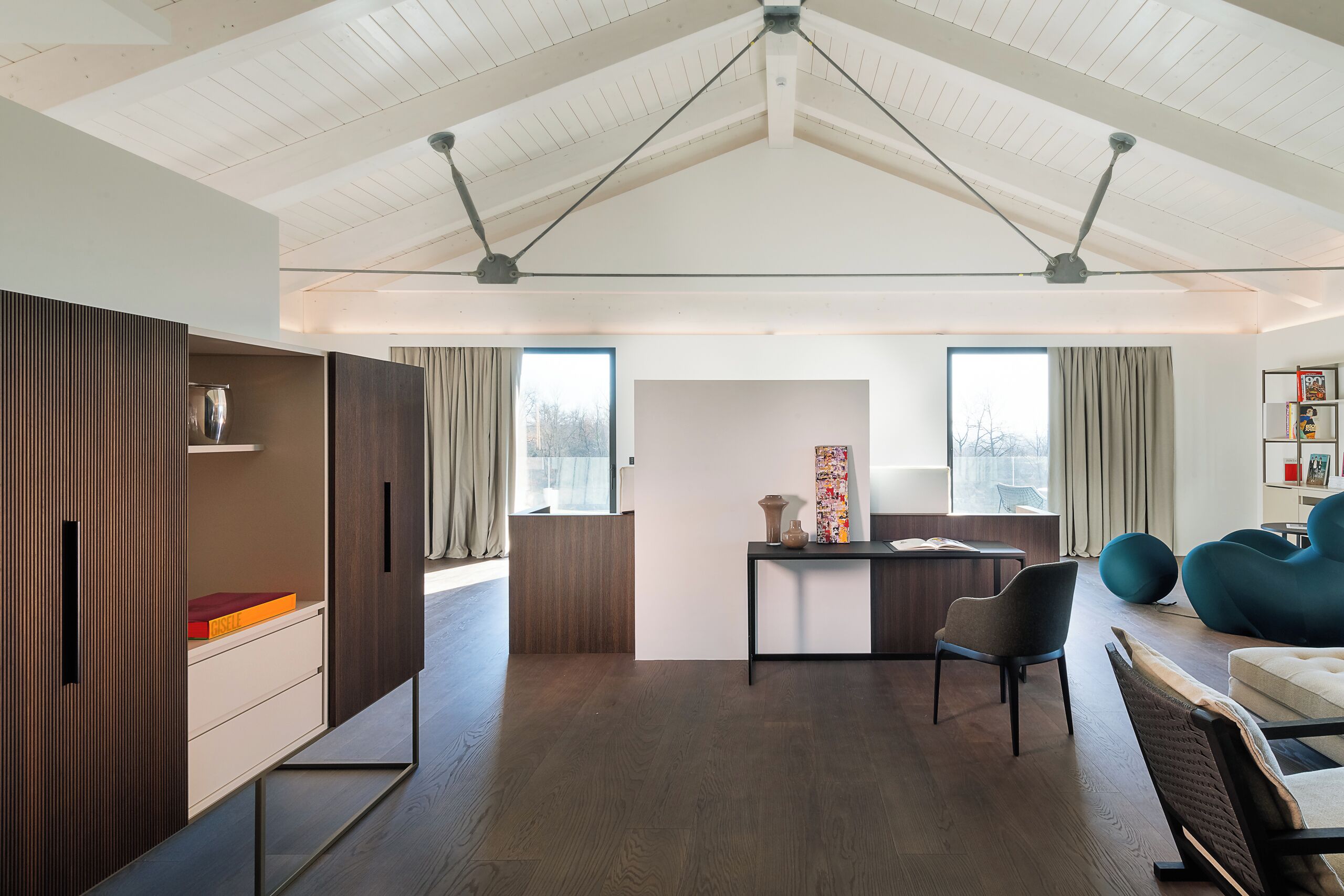 Una sala de estar moderna con piso de madera, un escritorio con una silla, un sofá y un ventanal con cortinas.