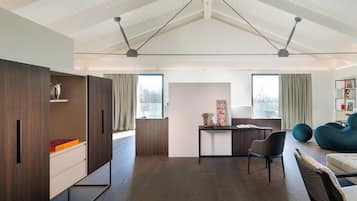 Una sala de estar moderna con piso de madera, un escritorio con una silla, un sofá y un ventanal con cortinas.