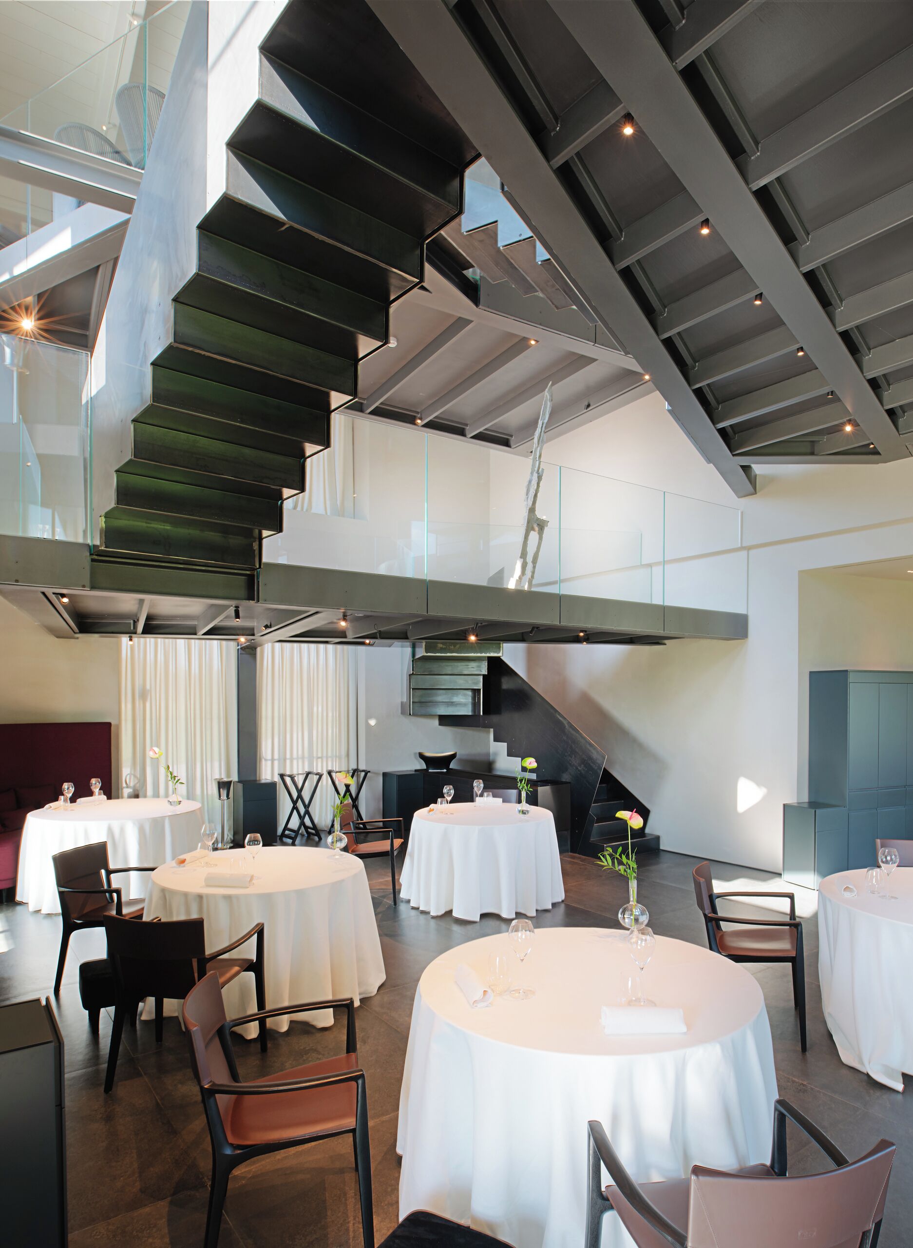 Ein moderner Essbereich mit runden Tischen, Stühlen und einer Treppe.