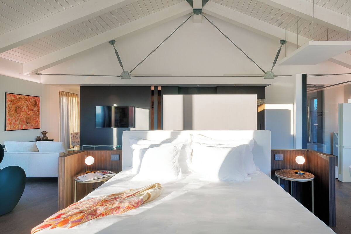 A modern hotel room with a large bed, bedside tables, a TV, and a ceiling fan.
