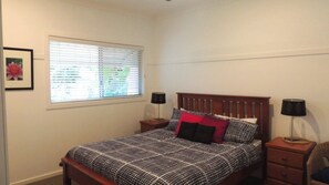 A bedroom with a bed, two bedside tables, a window with blinds, and a framed picture on the wall.
