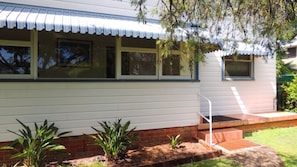 A single-story house with a front porch, a small garden area with plants, and a metal railing on the porch.